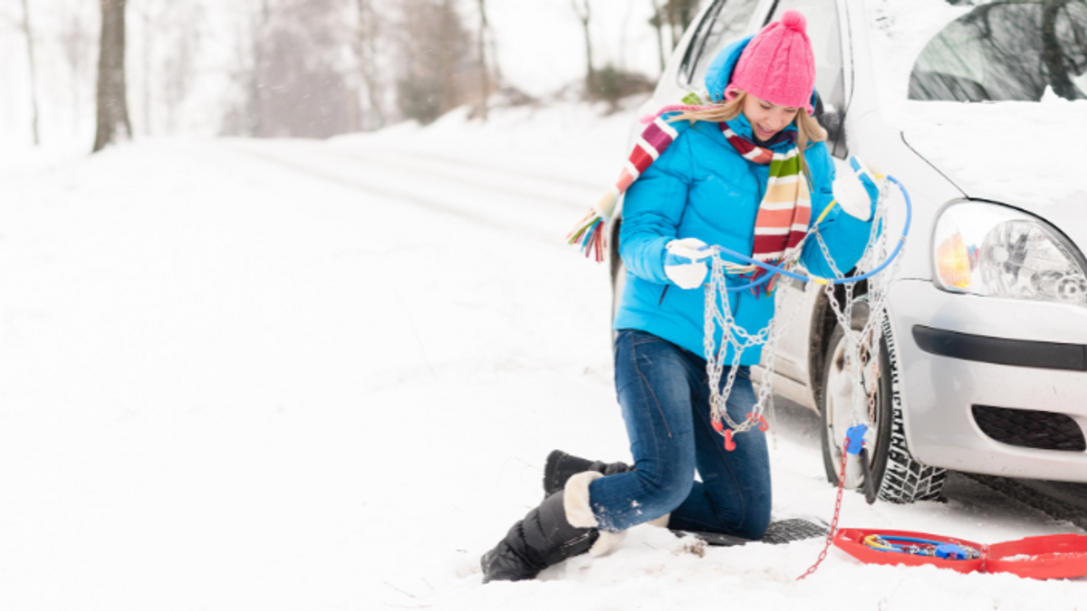 Frau montiert Schneeketten an ihr Auto